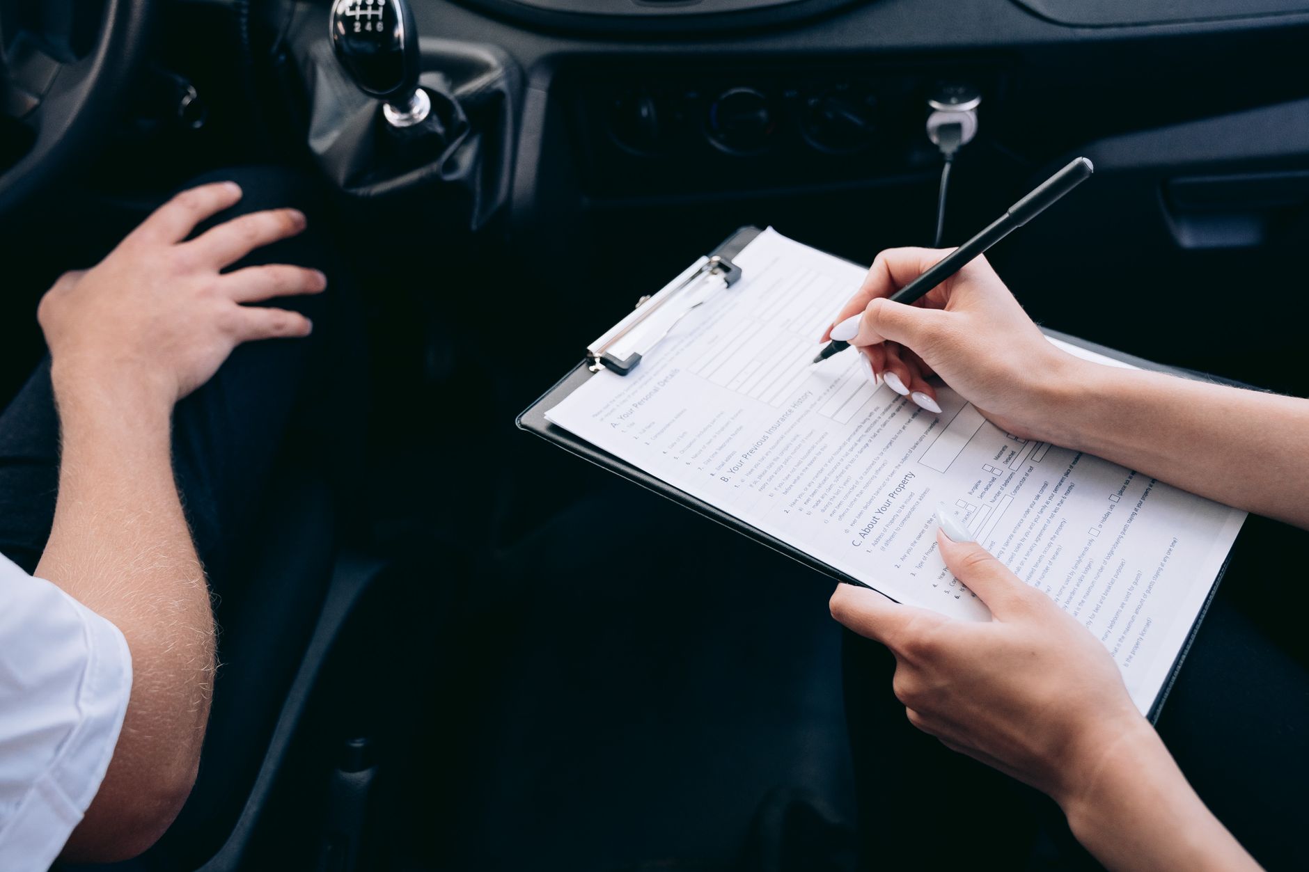 A person filling out paperwork in a car, the unglamorous side of driving that costs a new driver the most
