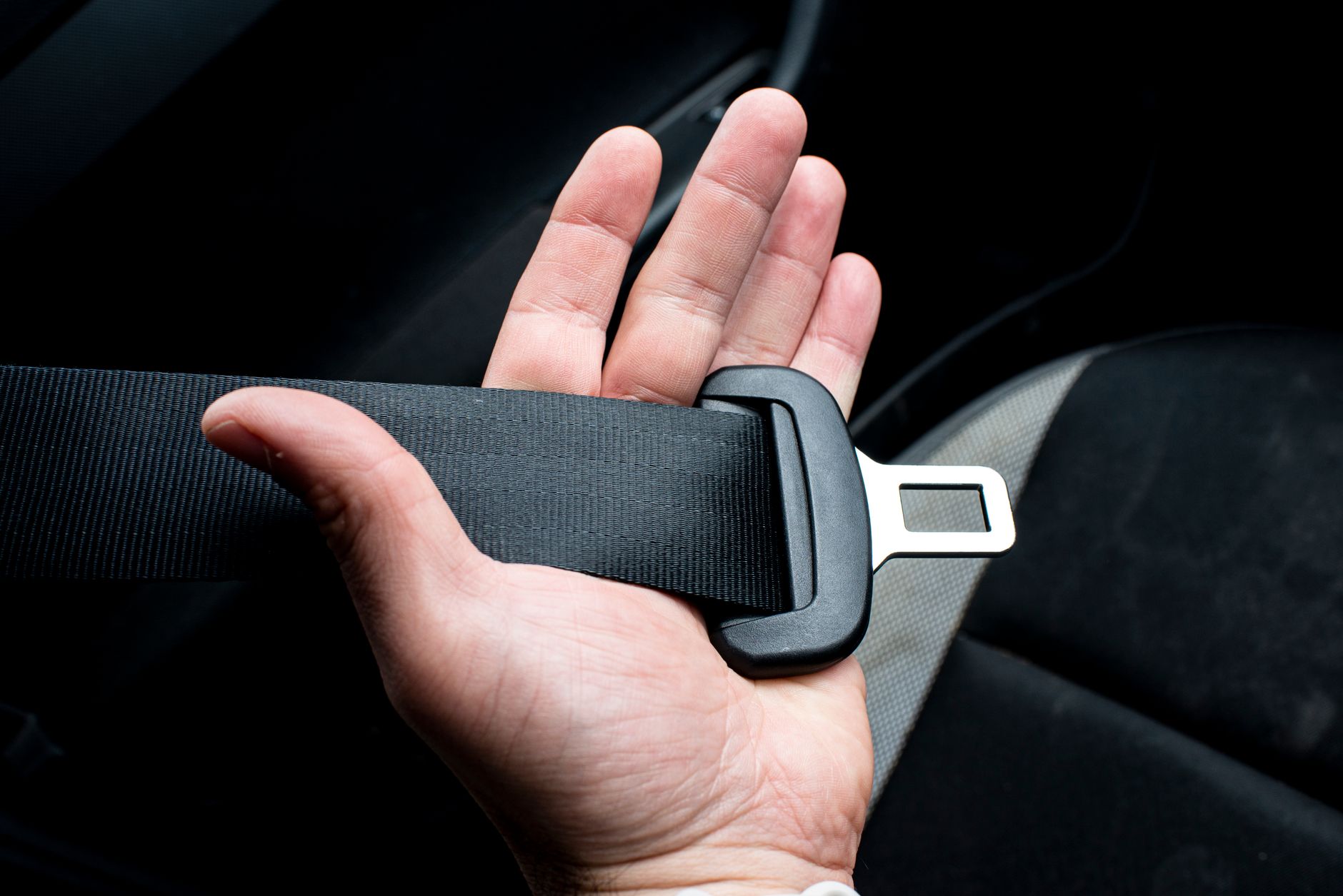 A hand holding a seat belt across the body, the one-second action that changes what a crash does to a person